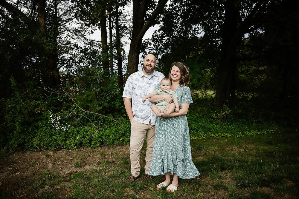 A family portrait of a man and woman standing next to each other and smiling as she holds her son for his birthday photoshoot in Medford, New Jersey.
