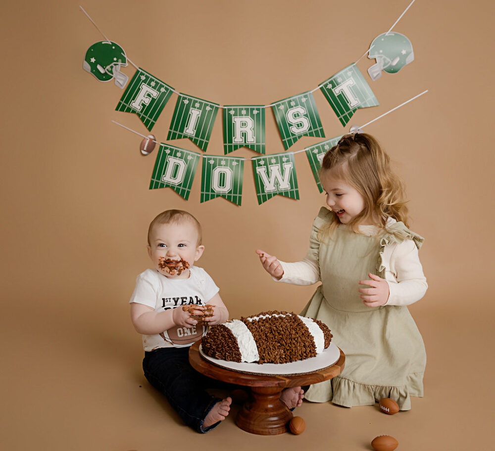 A sibling portrait of a boy and his bis sister sitting in front of a cake and eating for his first down first birthday session in Deptford, New Jersey.