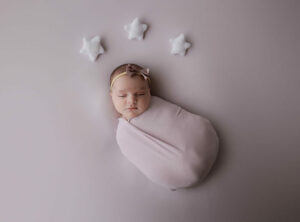 A cute picture of a baby sleeping during her professional baby photos, wrapped and adorned with felt stars by her head for a Lavender newborn session in Deptford, New Jersey.