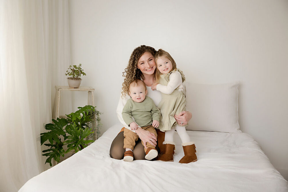 A familiy portrait of a mom and her two children wearing matching outfits and sitting on bed photography prop and smiling for a first down first birthday session in Southampton, New Jersey.