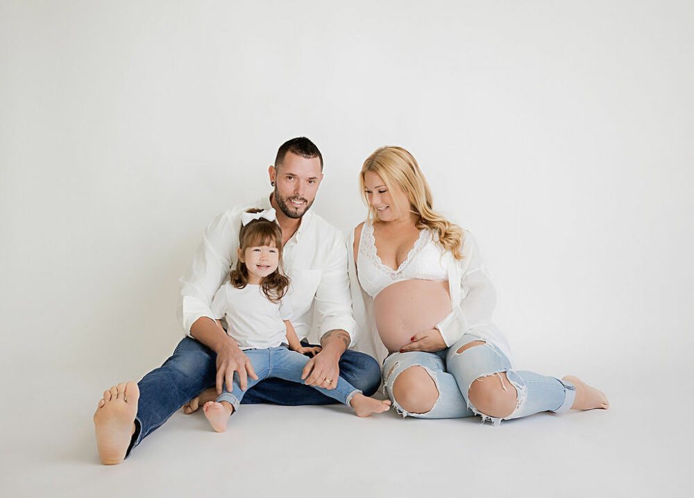 A beautiful photo of a family sitting on floor for a lifestyle portrait wearing denim and light colors during as formal maternity photoshoot in Westampton, New Jersey.