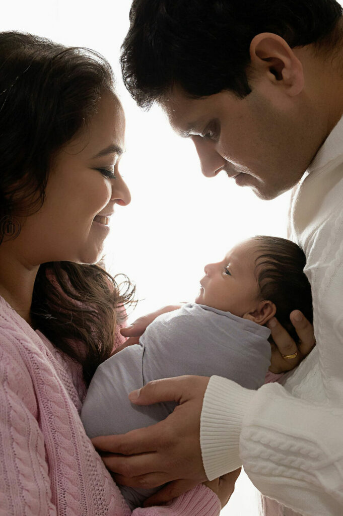 A beautiful portrait of a man and a woman looking down at their baby as they both hold him during his newborn session in Deptford, New Jersey.