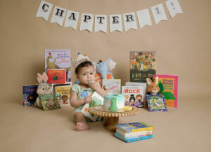 A cake smash photo of a boy eating his first birthday cake with several baby books as props for his backdrop for a book theme first birthday session in Deptford, New Jersey.