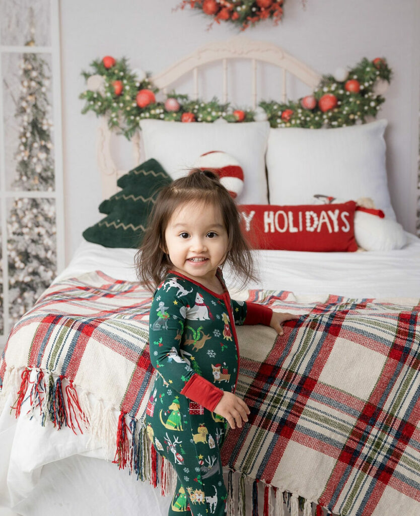 A close-up of a toddler girl smiling as she stands during her holiday mini sessions with a chritsmas theme in Delran, New Jersey.