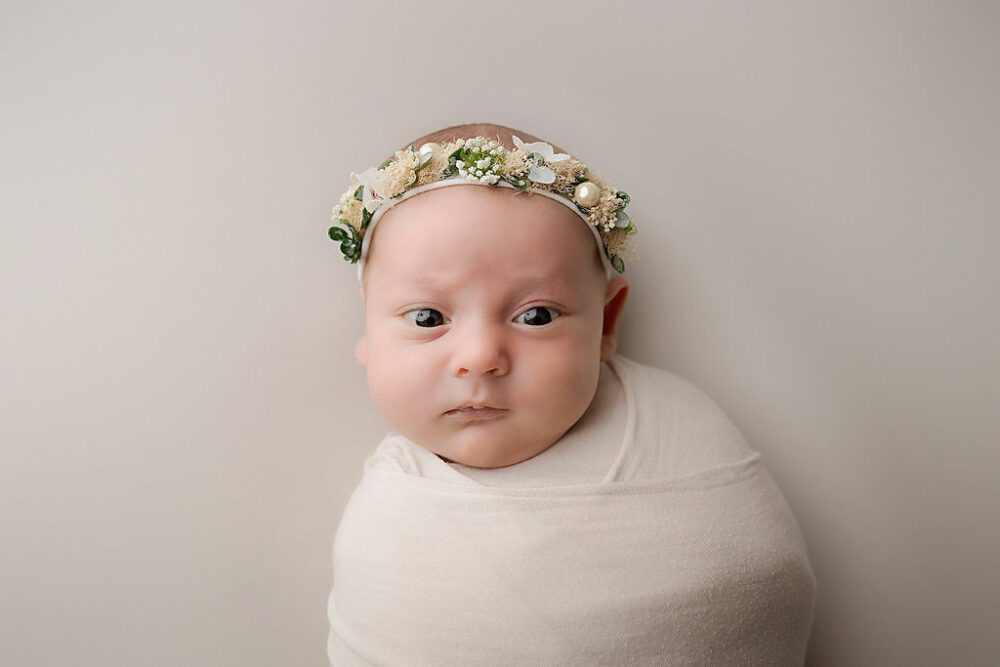 A close-up photo of a infant girl awake and swaddled, wearing cute headband for her professional pastel newborn session in Haddonfield, New Jersey.