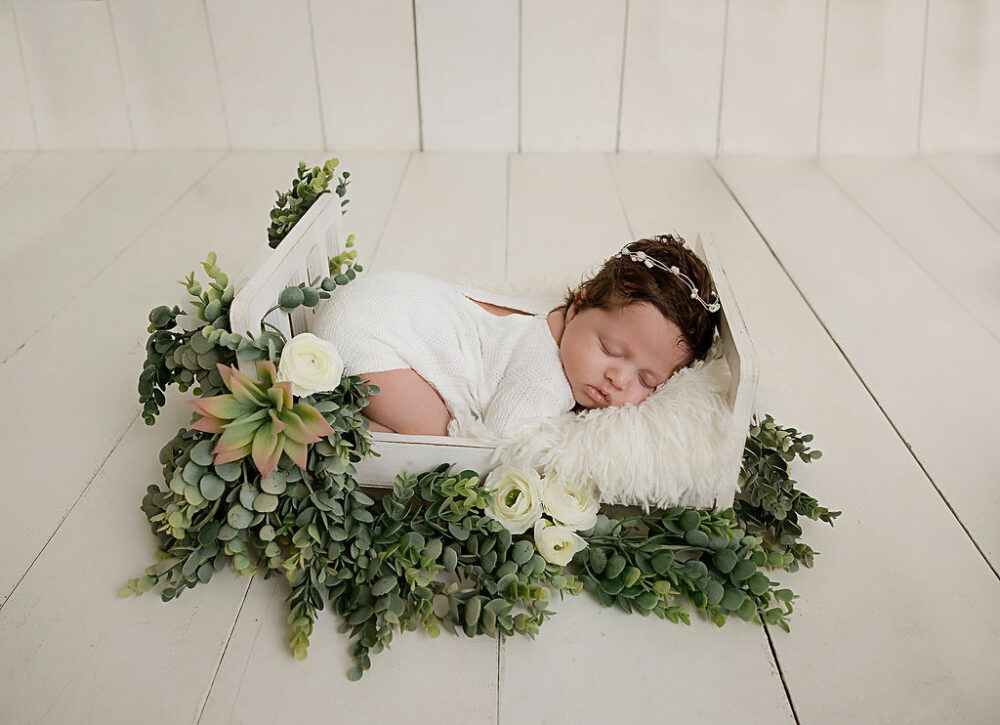 A beautiful photo of a sleeping baby girl in a tiny crib adorned with greenery fort her professional newborn photography in Delran, New Jersey.