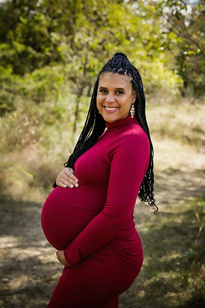 A beautiful pregnancy portrait of a woman wearing a body con long sleeve dress smiling and holding her belly for her professional red maternity session in Medford, New Jersey.