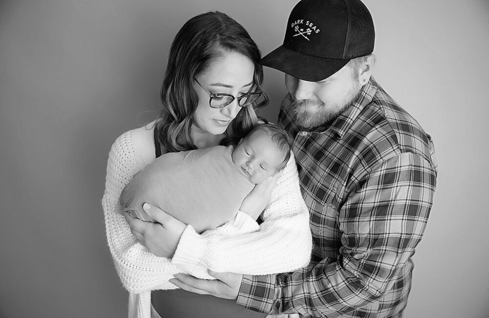 A cute photo of a woman and man smiling and holding their newborn for their warm maternity and newborn session in Southampton, New Jersey.