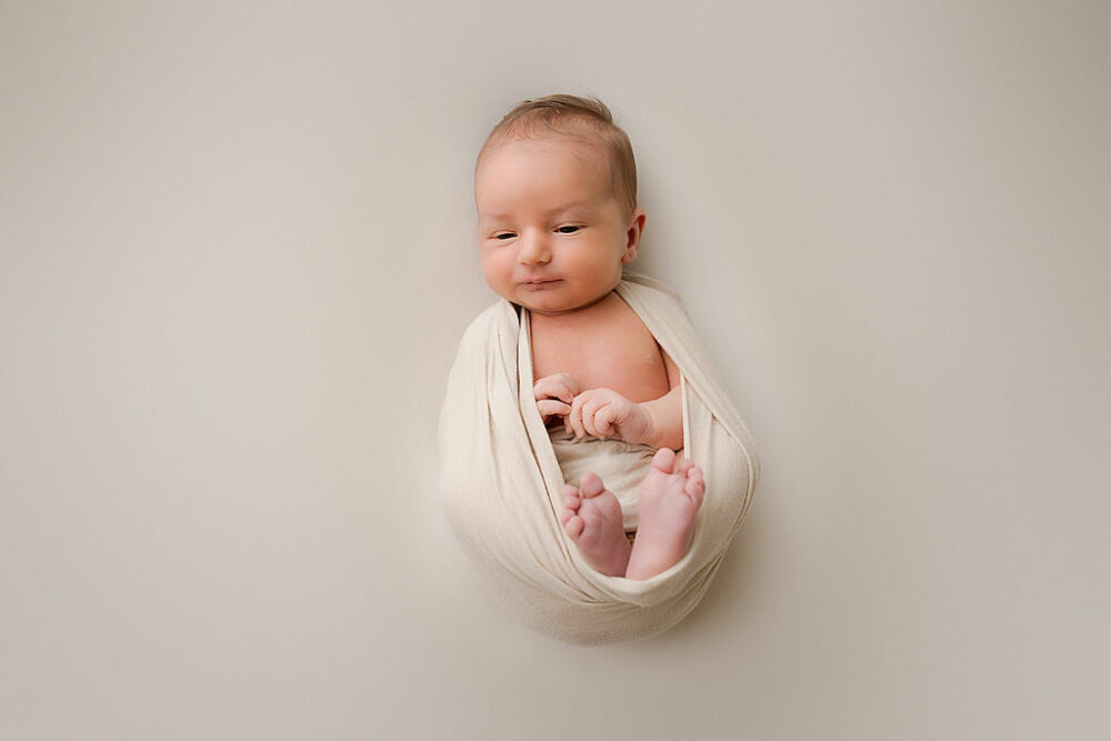 A newborn photo of a boy swaddled with his hands and feet peeking through for his professional warm newborn session in WEstampton, New Jersey.