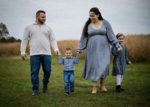 Beautiful family portrait of a woman and man holding the hands of there too children walking through a field for their moody outdoor family session in Burlington, New Jersey.