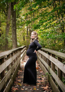 A woman standing on a wooden bridge in a lush farmstead posing and wearing dress for her maternity pictures taken in Delran, New Jersey.