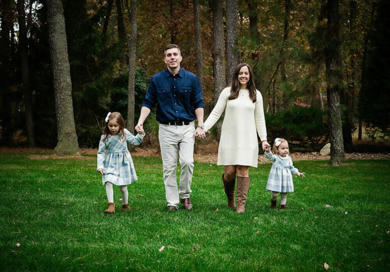 Beautiful photo of a man and women holding hands as they hold their daughters walking through a field wearing blue and white clothing for their fall family session in Deptford, New Jersey.